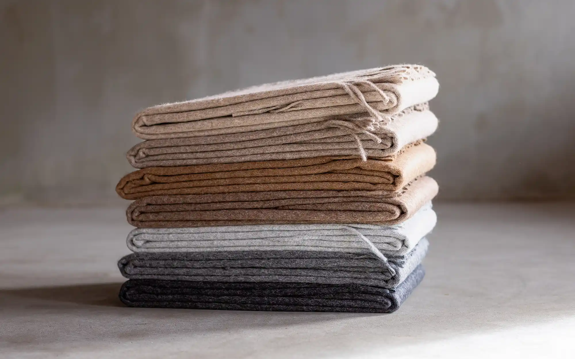 Zeven alpaca plaids stapelvormig gepresenteerd, perfect om de kleuren en texturen van het assortiment te laten zien