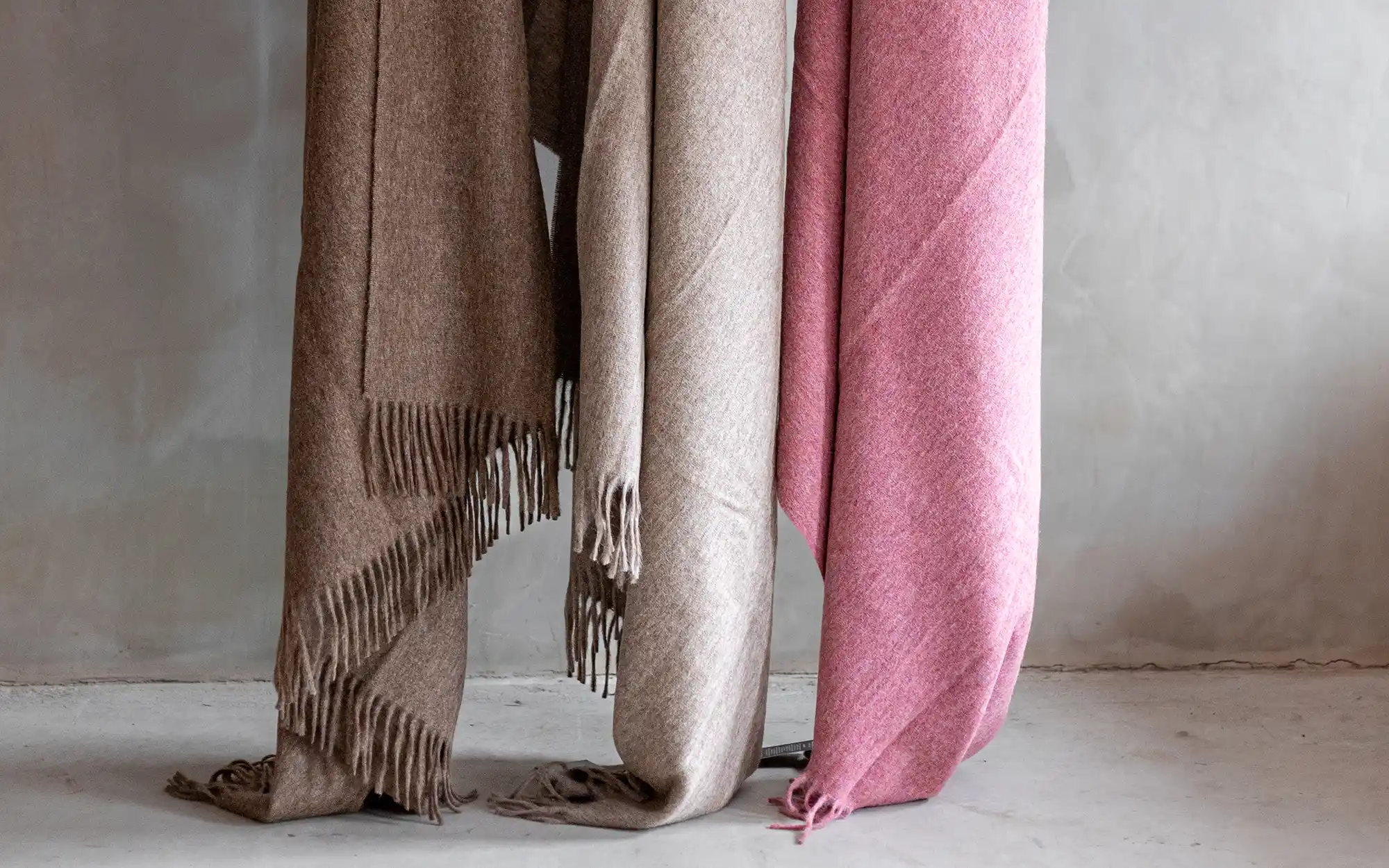 Drie zachte alpaca plaids in verschillende kleuren elegant hangend, ideaal voor een warme en stijlvolle inrichting