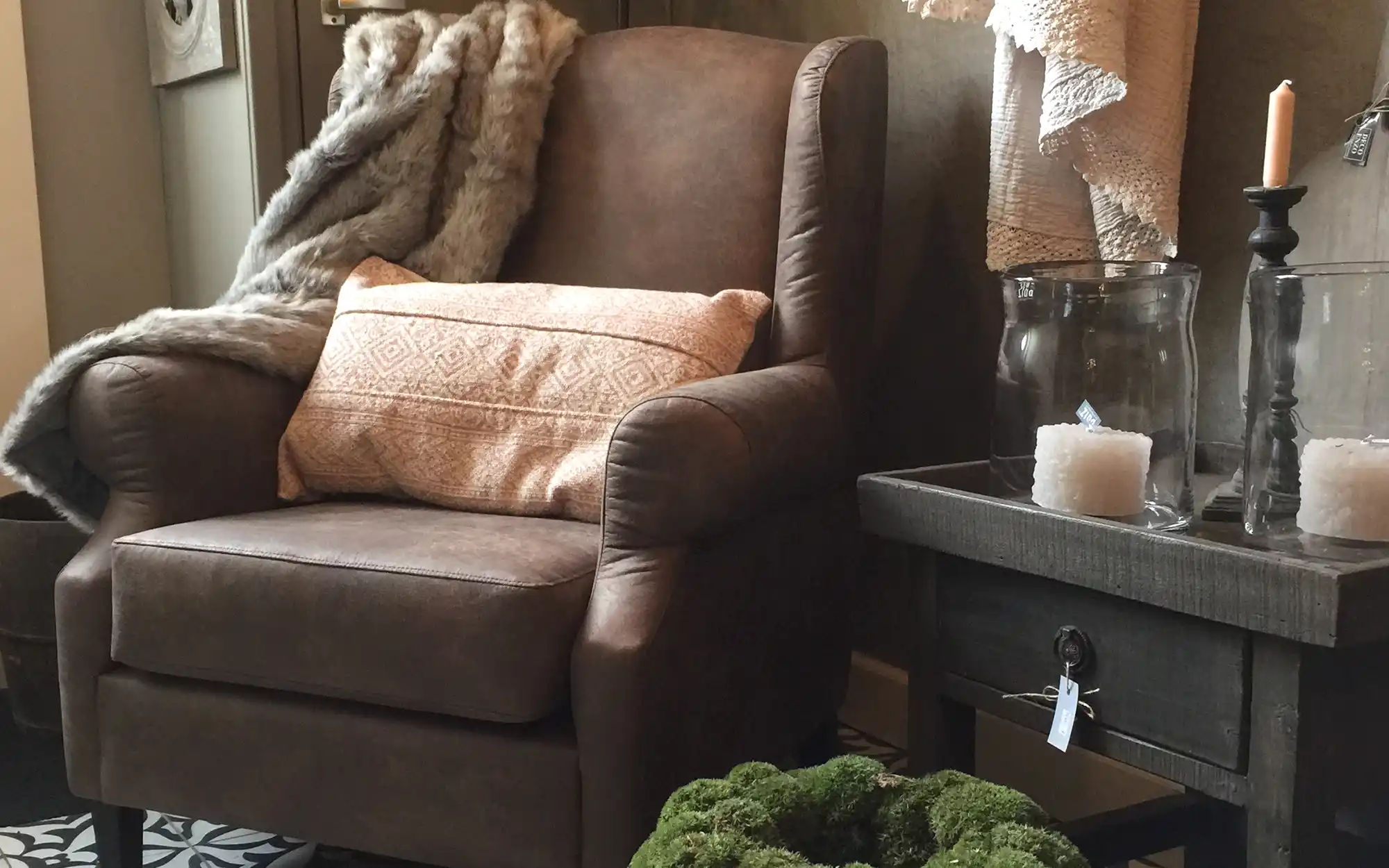 Klassieke oorfauteuil Fleur in donkerbruine stof, gestyled met plaid en sierkussen.